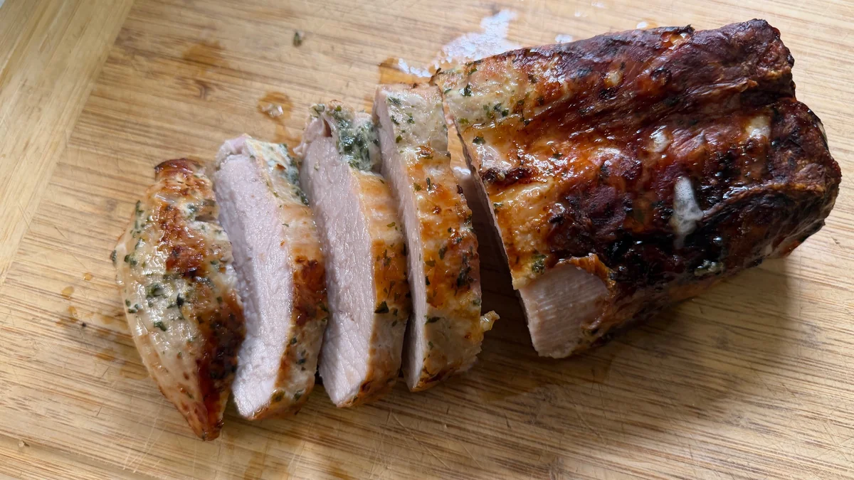 Sliced garlic herb pork loin on a wooden cutting board, photographed in Sofia's kitchen