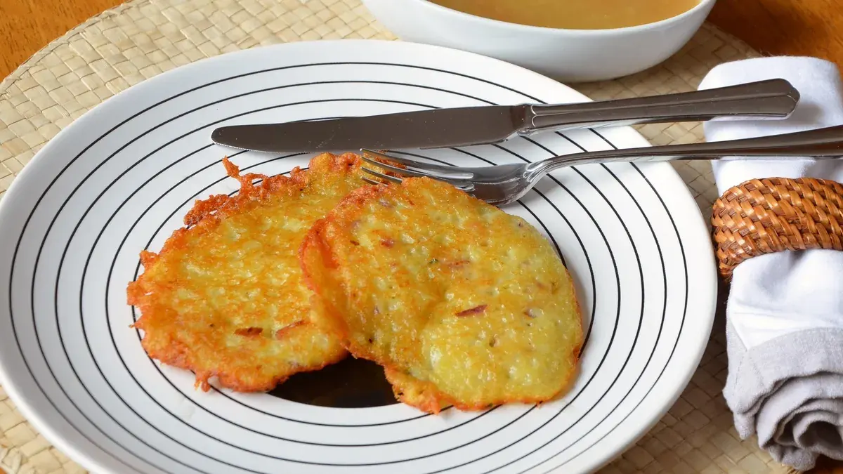Crisp potato latkes on a plate with a bowl of applesauce