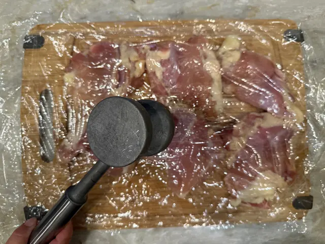 Pounding chicken thighs flat between sheets of plastic wrap