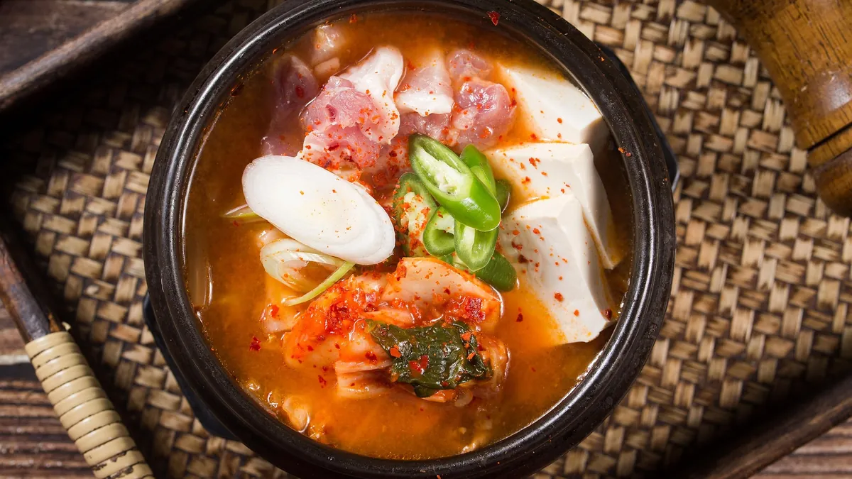 Kimchi stew with pork, tofu, green chile and green onion in a black earthenware pot