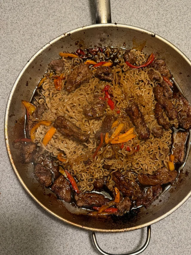 Seared flank steak, ramen noodles and sliced sweet peppers tossed in the sauce in a stainless skillet