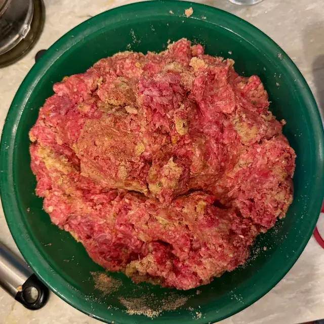 Ground beef, bread crumbs and onion-mushroom soup mix being combined in a green mixing bowl