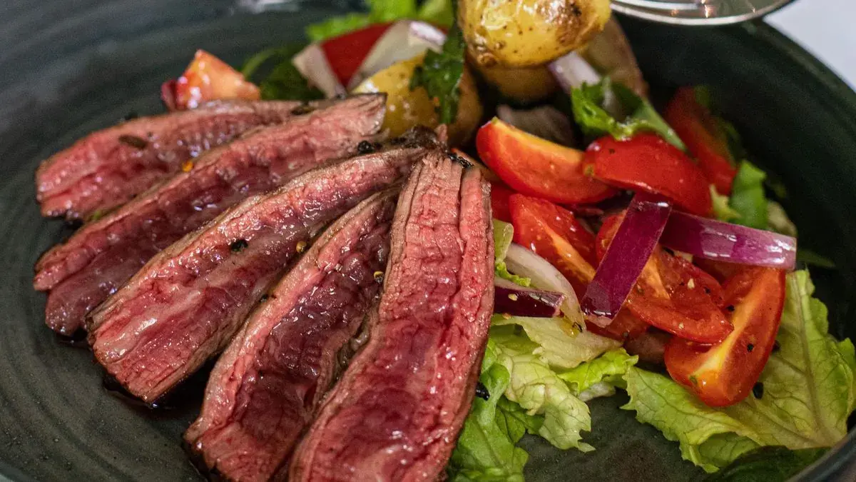 Sliced medium-rare steak over a tomato and lettuce salad
