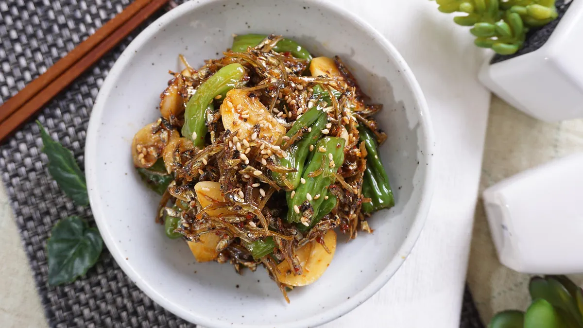Stir-fried anchovies with shishito peppers, garlic and sesame seeds in a white bowl