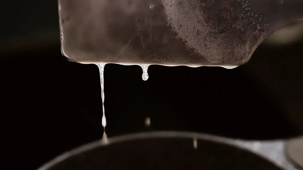 Rendered chicken fat dripping from a spatula into a pot of schmaltz