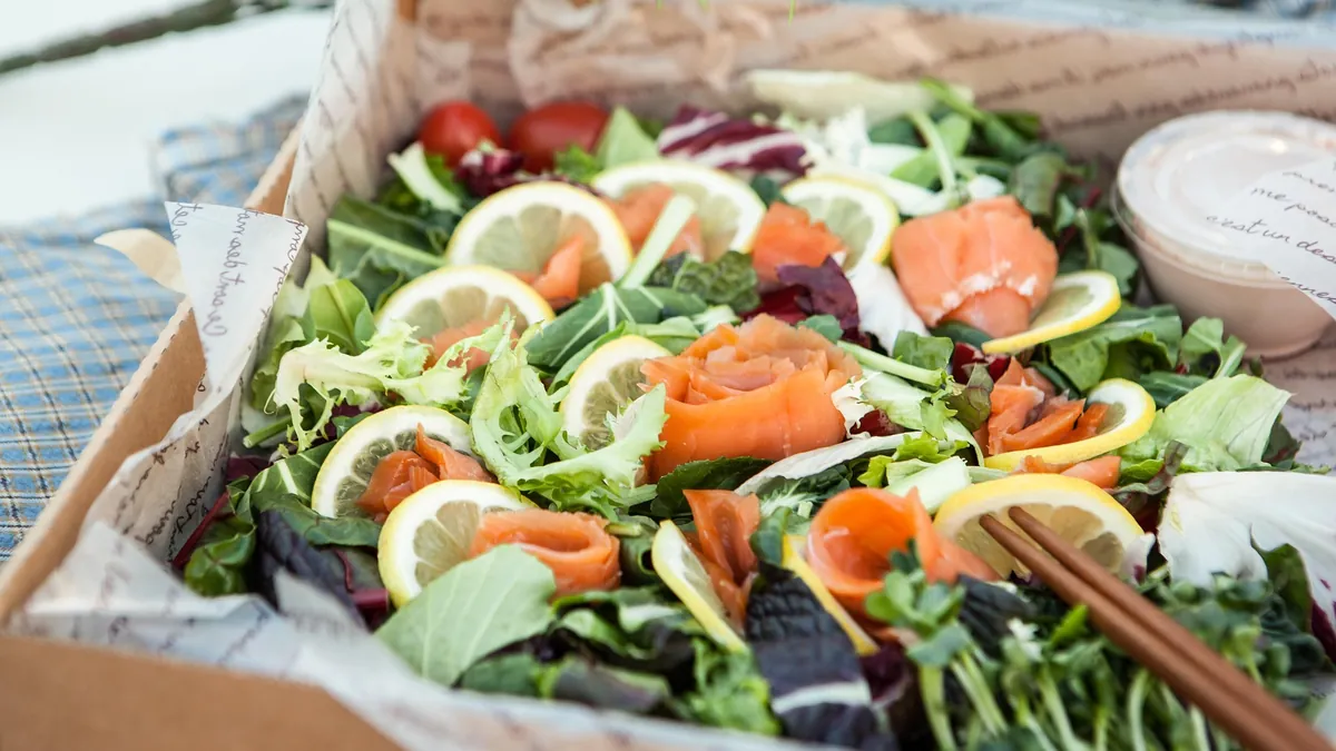 Smoked salmon rosettes with lemon slices, mixed greens and cherry tomatoes in a picnic box